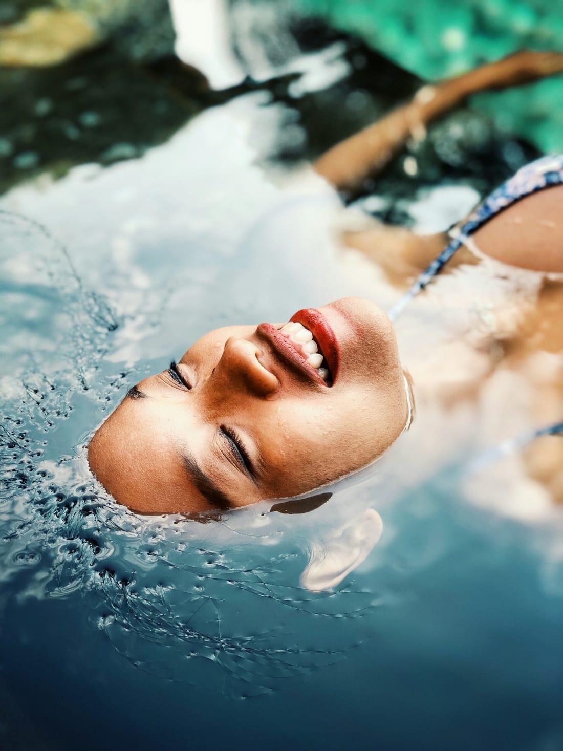 Woman floating calmly in clear water, eyes closed and smiling